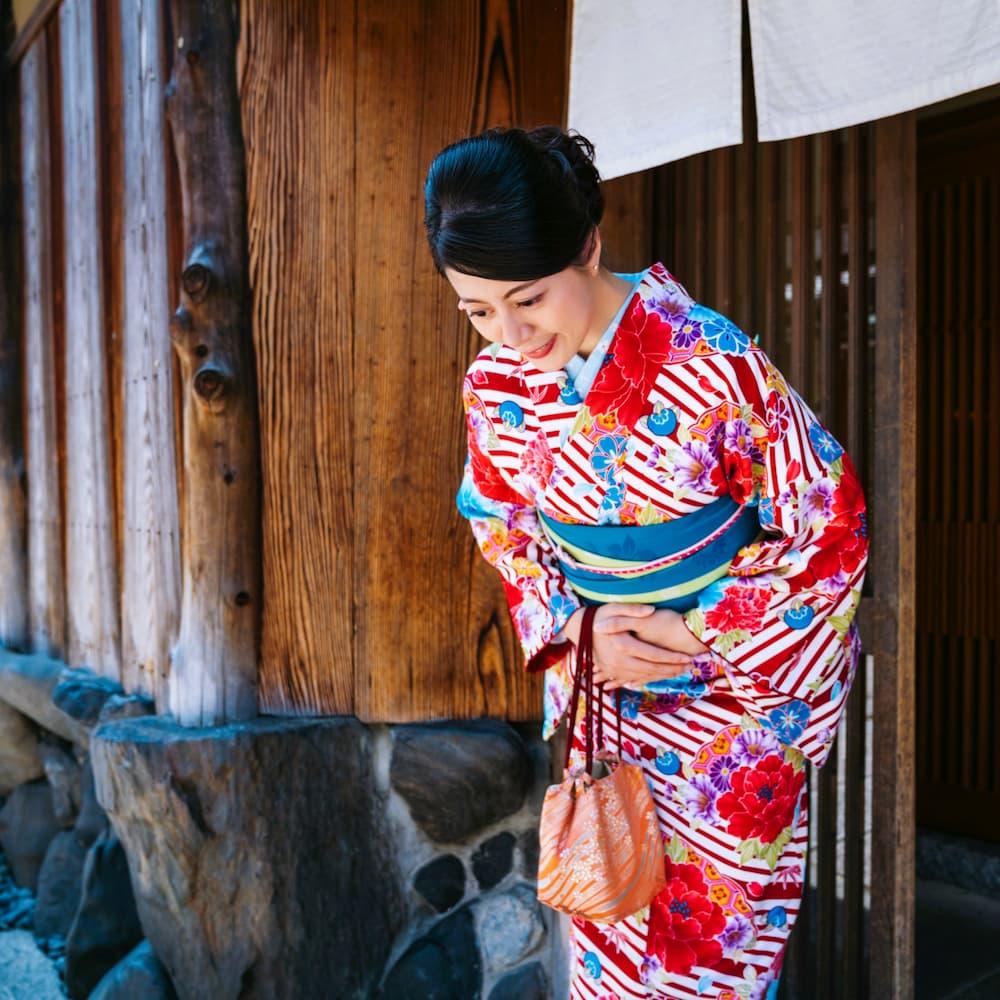 Japanische Frau in einem bunten Kimono verbeugt sich vor einem traditionellen Holzgebäude in Kyoto