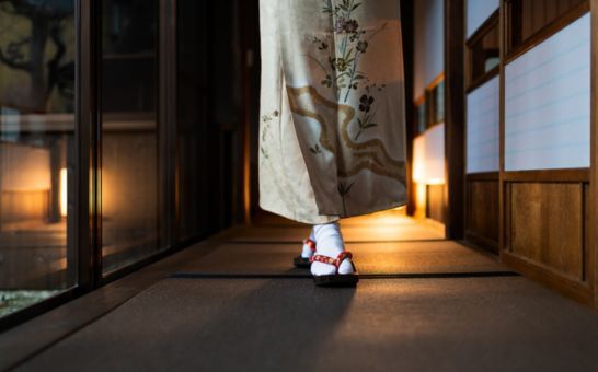 Frau im Kimono geht durch einen traditionellen Ryokan mit Tatami-Matten und Shoji-Türen