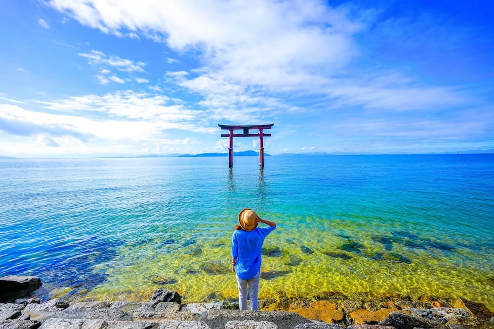 Ein Reisender steht in der Nähe eines Torii-Tors am Biwa-See in der Präfektur Shiga, Japan