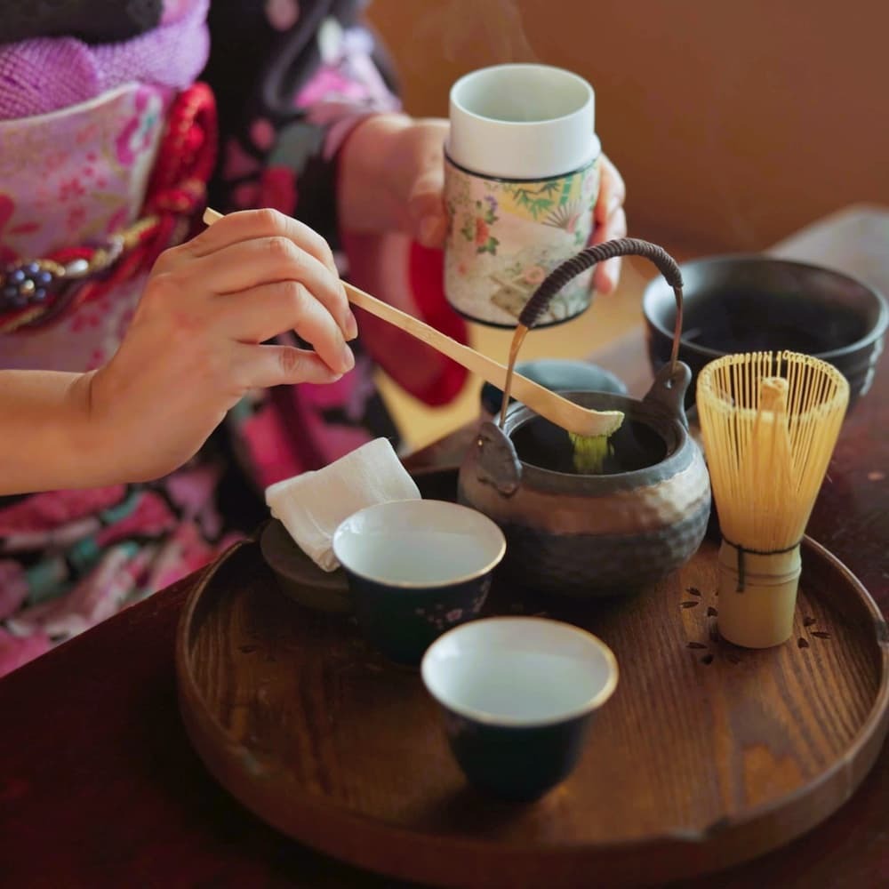 Japanische Frau bei der Zubereitung von Matcha-Tee in einer traditionellen Teezeremonie zu Hause, mit Matcha-Pulver, Kräutern und einer Teekanne