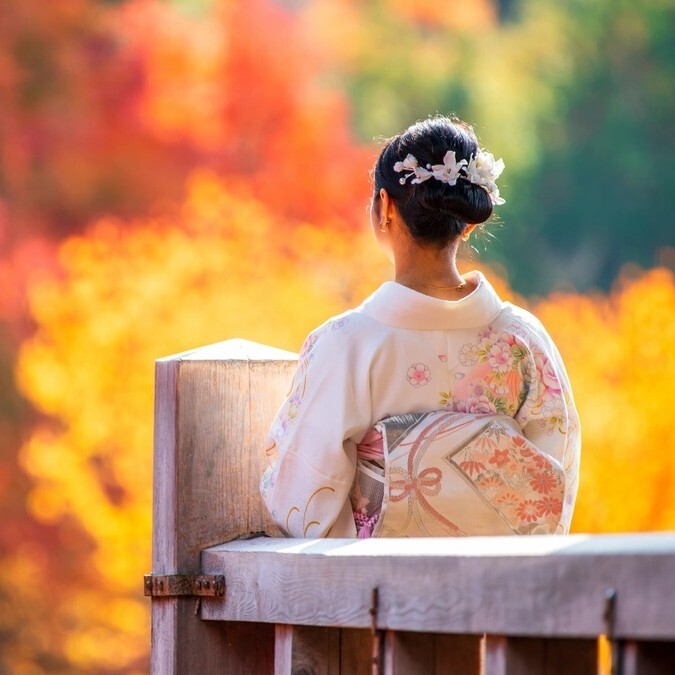 Frau im Kimono blickt auf Herbstlaub in Japan